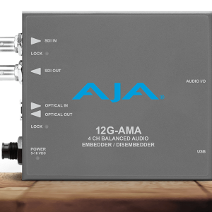 Procesador de audio profesional AJA 12G-AMA en chasis gris, con leyendas blancas que indican la entrada y salida de vídeo SDI, conectividad USB y el puerto de audio balanceado de cuatro canales.