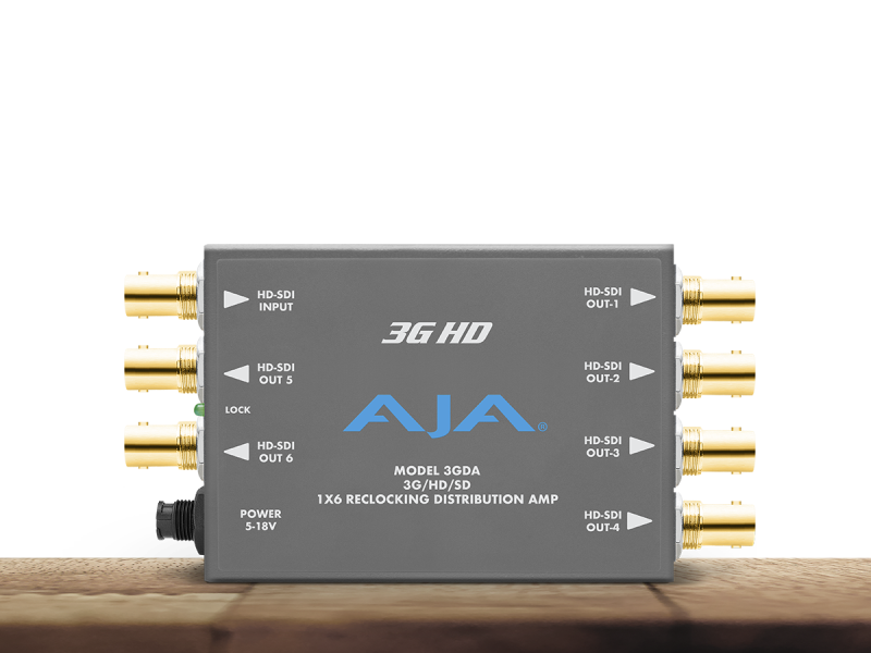 Amplificador distribuidor AJA 3GDA para vídeo profesional en chasis metálico gris, con siete conectores BNC dorados de alta calidad, LED de bloqueo de señal y entrada de alimentación circular.