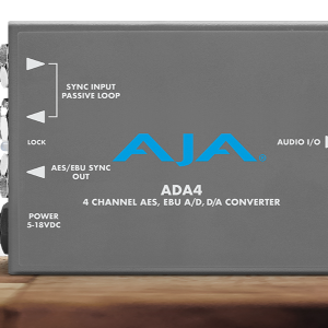 Conversor de audio profesional compacto AJA ADA4 en chasis gris oscuro, mostrando tres conectores BNC para sincronización y salida AES/EBU, puerto USB de configuración y conexión de alimentación circular.